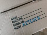 Cardboard box labeled with room destination for kitchen during moving process.