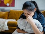 A woman sitting indoors, holding a blanket, conveying emotions of stress and contemplation.