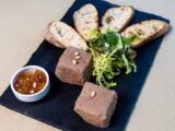 Delicious liver pâté with toasted baguette, salad, and chutney on a slate serving board.