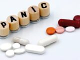 Assorted pills arranged beside wooden tiles spelling 'PANIC', symbolizing anxiety treatment.