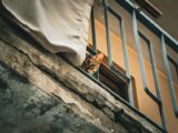 A curious Bengal cat peers from a balcony in an urban setting, highlighting feline curiosity and urban life.