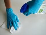Close-up of hands wearing gloves cleaning a surface with disinfectant spray.